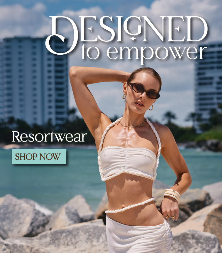 Woman in a white bikini standing on rocks with a cityscape and ocean in the background, promoting resortwear.